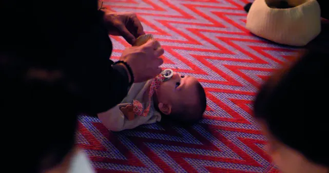 Un bébé couché sur un tapis découvre le mouvement et les sons fait pas une adulte à l'aide d'un instrument