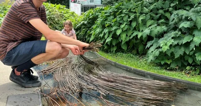 Un homme est penché sur un plan d'eau dans lequel se trouve des branches de saule devant le Musée d’ethnographie