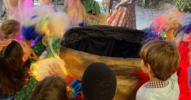 Deux membrex de Genevegas,  Iconyx et Amber autour d'un chaudron magique. Des enfants les regardent ébahis.