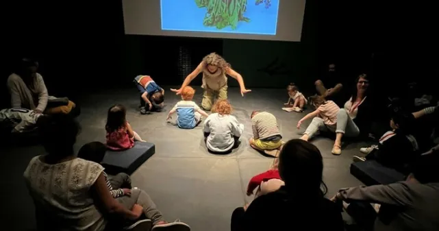 Quelques enfants et adultes sont devant une artiste et font des gestes avec leurs bras