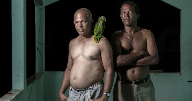 Photographie prise dans le village d'Helvécia deux frères qui pose de face. L'un deux porte un oiseau vert sur l'épaule.